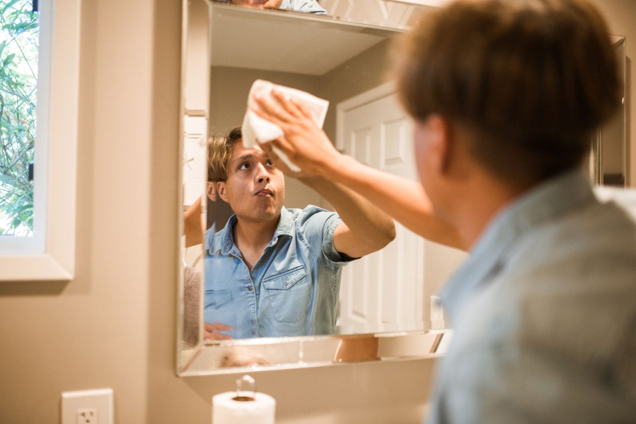 who-we-are A man wiping a bathroom mirror, focusing on cleanliness and hygiene in a domestic setting.